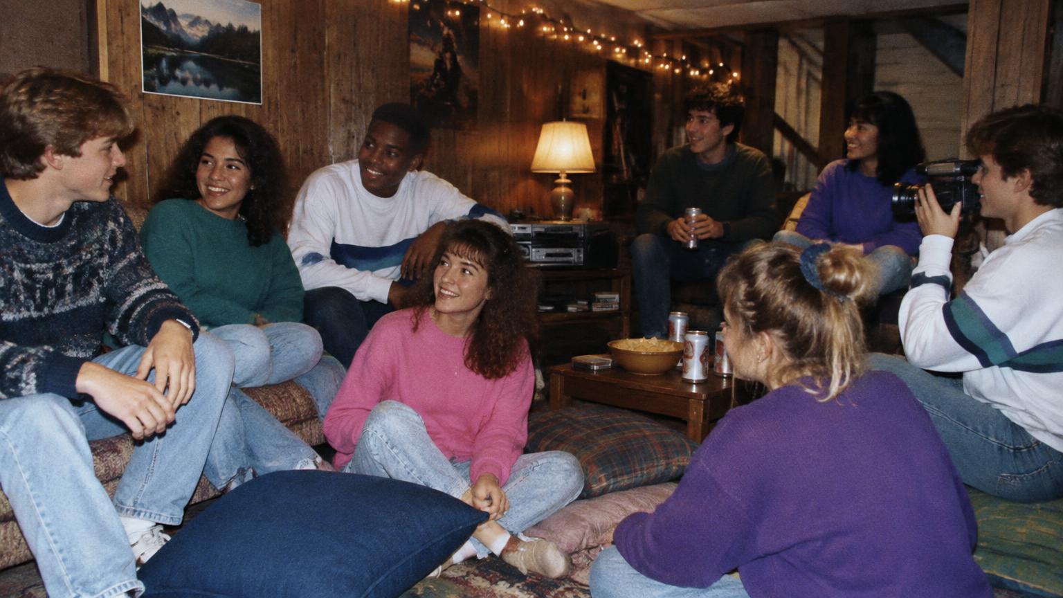 Seniors on floor pillows at a basement party while a friend films with a camcorder